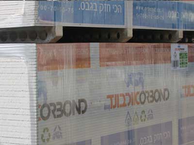 ערמת לוחות גבס ארוזים בניילון על משטחים, עם הלוגו Corbond ושלט בעברית בחלק העליון